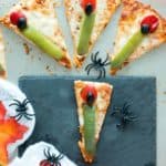 Slices of vegetarian pizza topped with spooky witch fingers made of green peppers, red peppers and black olives.