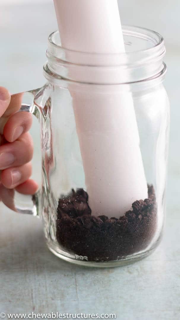 Inside a transparent mason jar there are crushed Oreo cookies and a rolling pin with no handles.