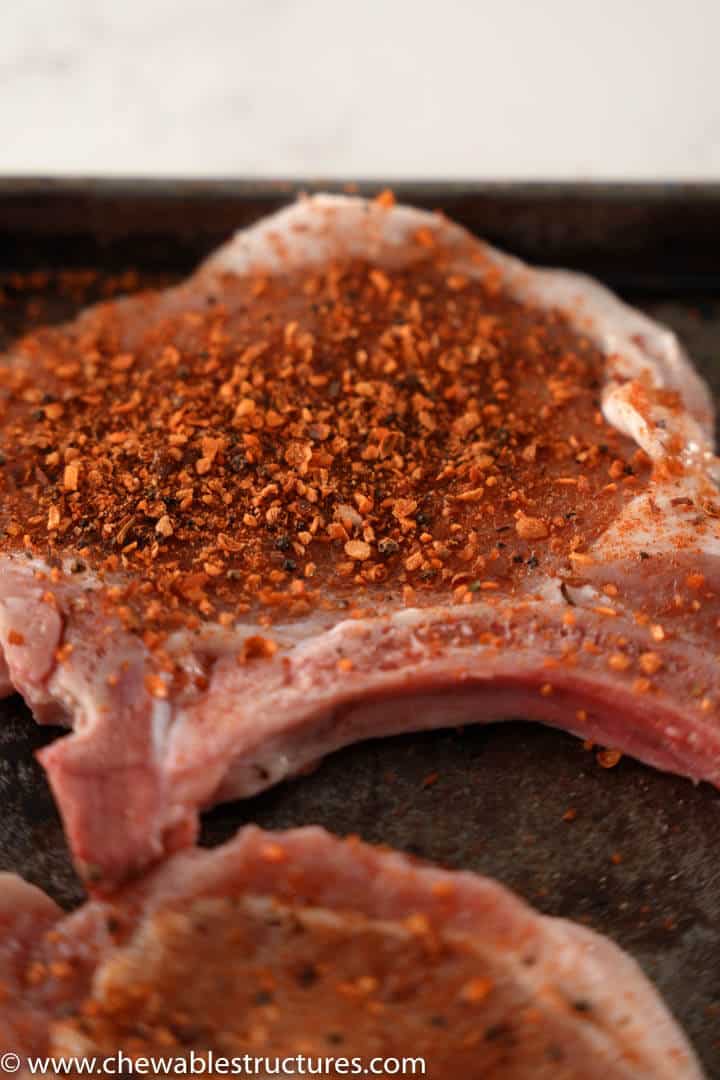 thin, centre cut bone-in raw pork chops covered in McCormick Chipotle & Roasted Garlic Seasoning on a baking sheet