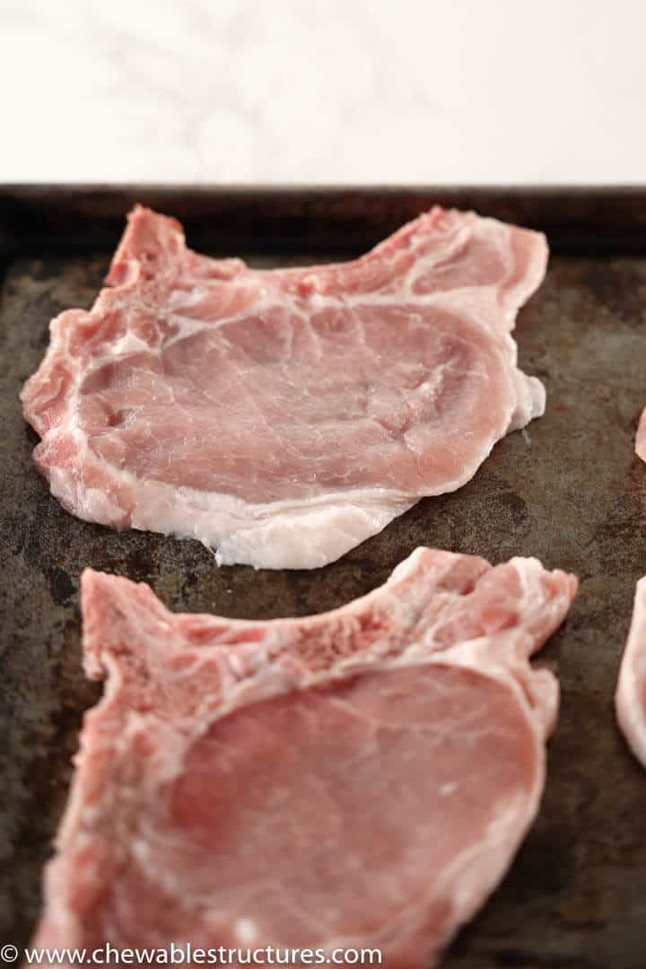 2 thin, centre cut bone-in raw pork chops on a baking sheet