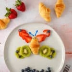 butterfly made of a mini croissant, strawberries, kiwis and blueberries on a plate