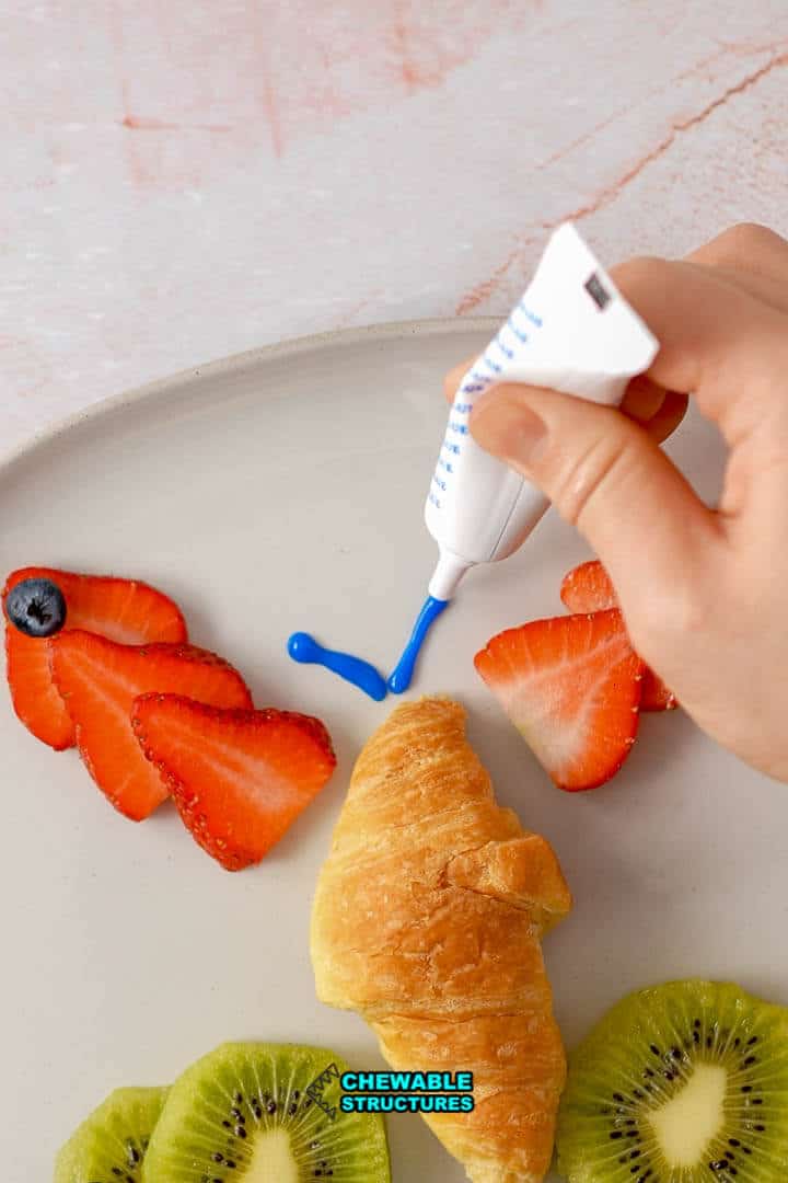hand drawing antenna on a croissant shaped-like a butterfly using blue icing